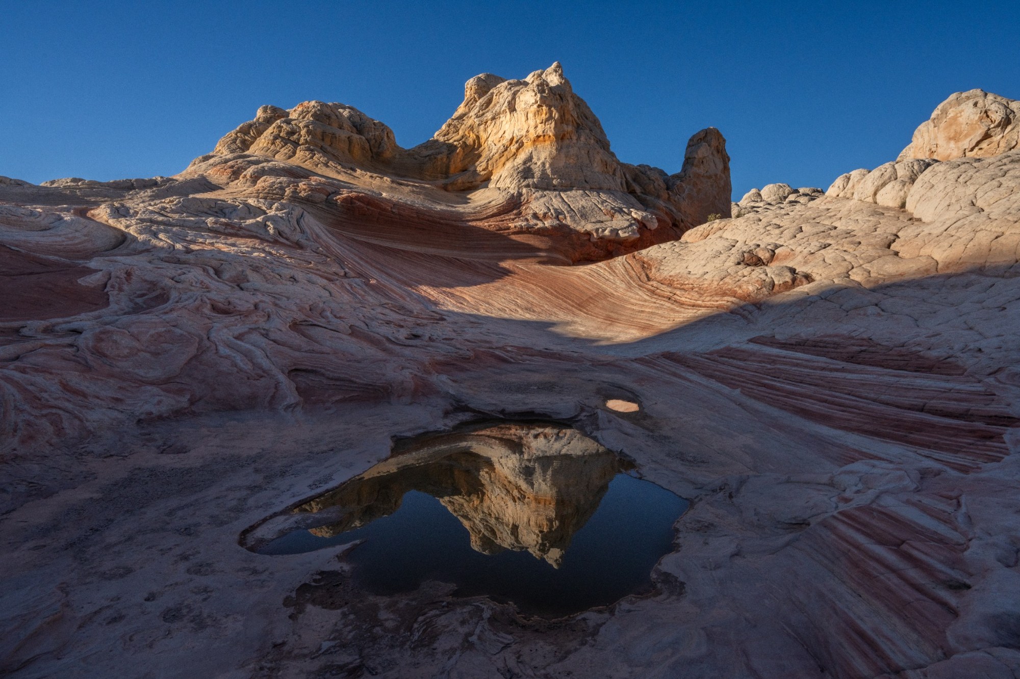 Layered pale sandstone formations and a pool under blue sky